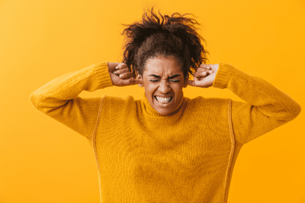 A woman being triggered and using her hands to cover her ears so she doesn't hear anything.